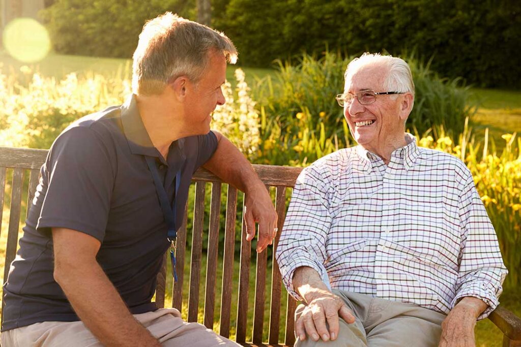 Older adults and a family member review bills, benefit papers, and a monthly budget at a kitchen table.